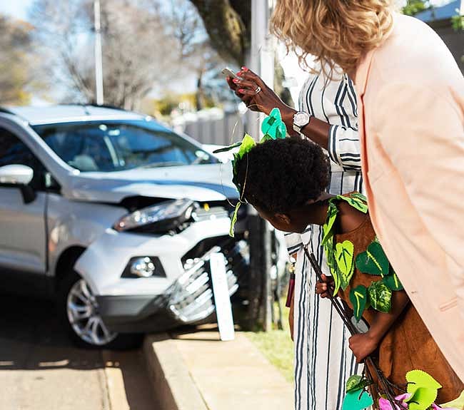 Women and a girl looking at an accident damaged car