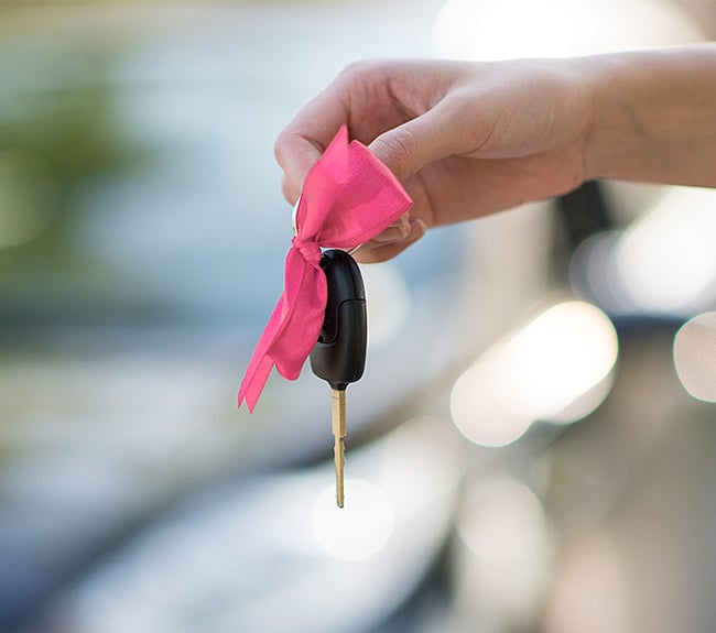 Hand holding car keys with a pink ribbon