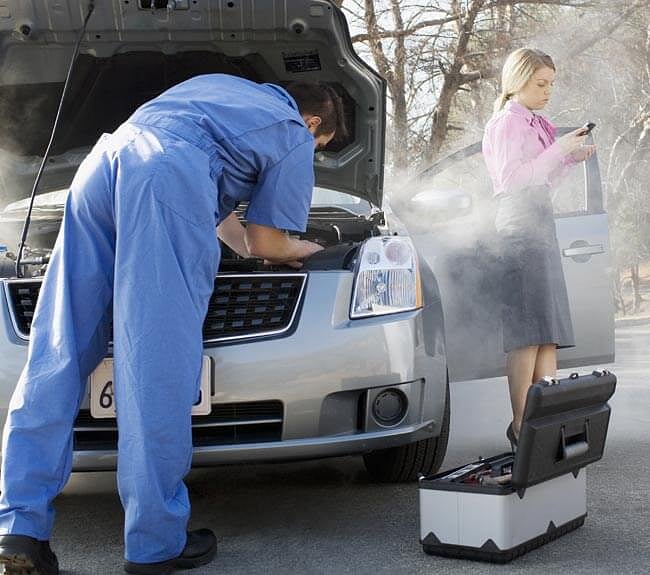 Mechanic fixing a smoking car while a woman stands by